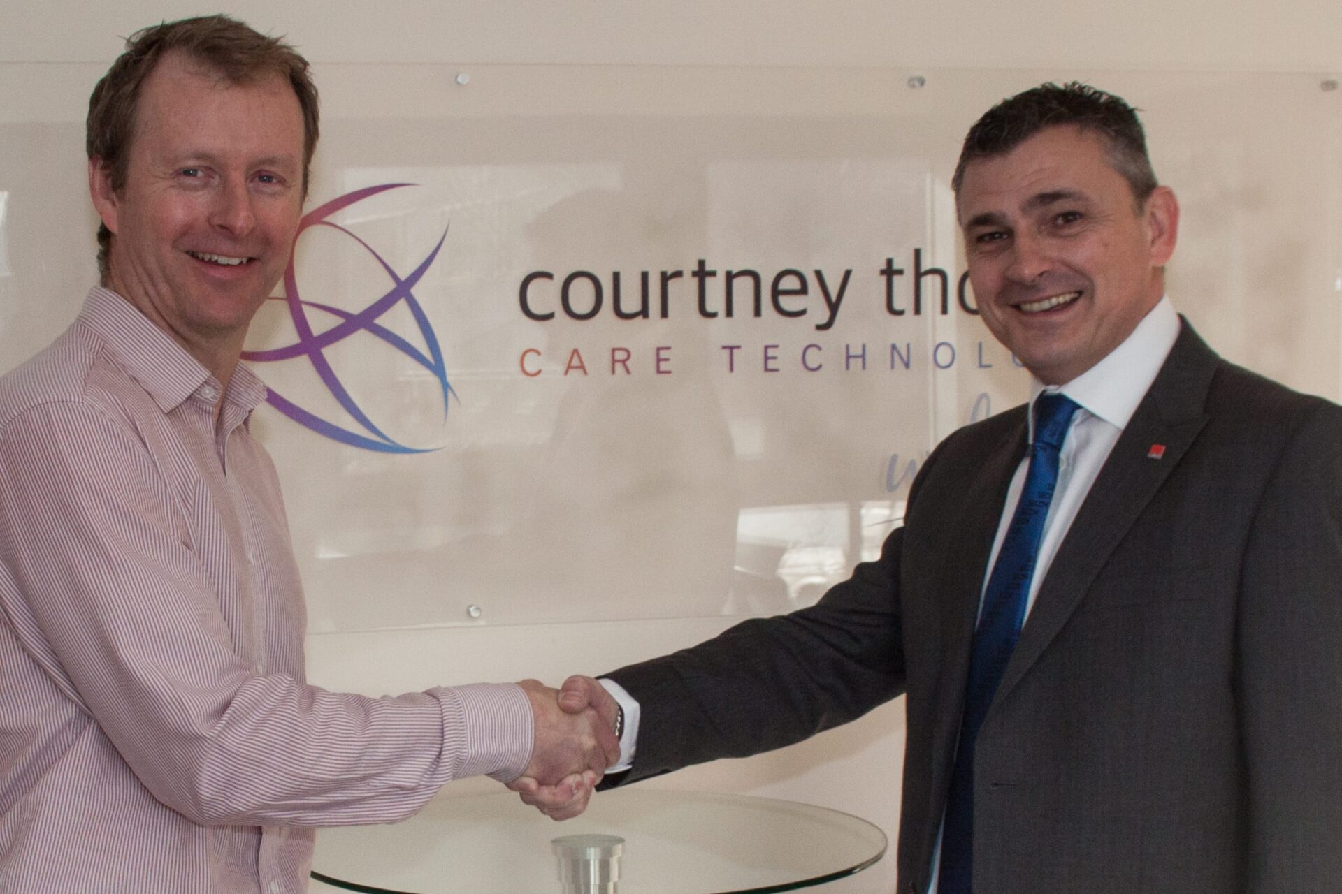 courtney-thorne-healthcare-banners-in-background-courtney-thorne-and-secom-in-front-of-desk-with-case-studies-talking-about-partnership-shaking-hands